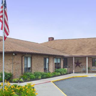A single-story brick building with an American flag in the foreground and landscaped greenery.