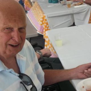 An elderly man sitting at a table indoors with food and sunglasses.