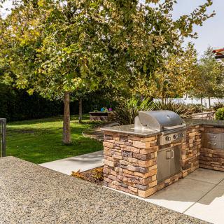 A well-maintained backyard featuring a stone barbecue grill and lush greenery.
