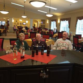A group of elderly people seated at a table in a restaurant, with bottles on the table.