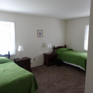A simple bedroom with two twin beds featuring green bedding, furnished with nightstands and lamps.