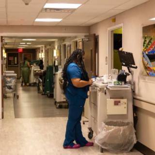 A nurse in blue scrubs works at a medical station in a hospital corridor.