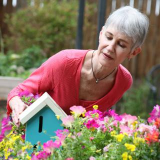 A woman tending to a colorful garden with a small birdhouse.