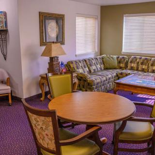 A cozy living room with a patterned sofa, round wooden table, and chairs, complemented by a lamp and decorative items.