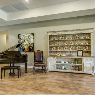A cozy living room featuring a grand piano, a display cabinet with decorative plates, and elegant artwork.