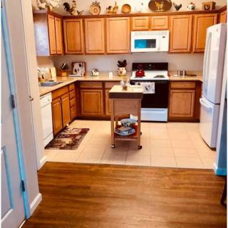A cozy kitchen with wooden cabinets and modern appliances, featuring a small island cart and decorative plates displayed above.