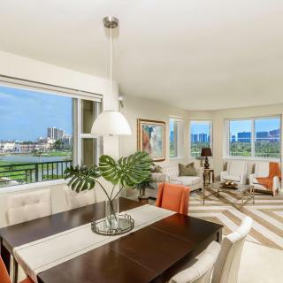 A modern living and dining area with large windows offering a city view, filled with natural light and decorated in neutral tones.