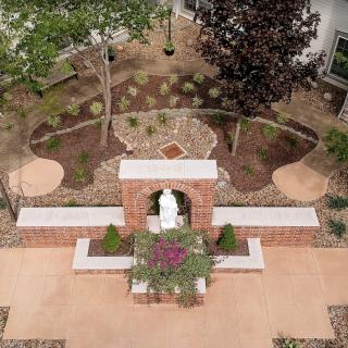 A beautifully landscaped garden with a central statue and surrounding pathways, viewed from above.