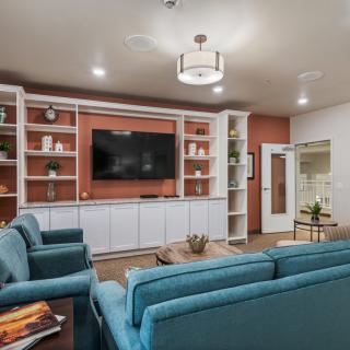 A modern living room with blue sofas, wall-mounted television, and built-in shelving units.
