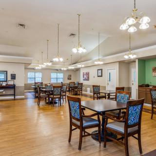 A spacious dining area with wooden floors, tables, and chairs under elegant lighting.