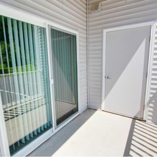 A sunny balcony with a sliding glass door and vertical blinds.