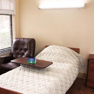 A cozy room featuring a bed, chair, and side table, designed for comfort in a healthcare setting.