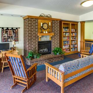 A cozy living room with a brick fireplace, wooden furniture, and a bookshelf.