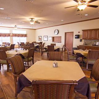 A cozy dining room with neatly arranged tables and chairs, featuring wooden flooring and ceiling fans.