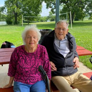 An elderly couple sitting on a bench in a park, enjoying a relaxing day outdoors.