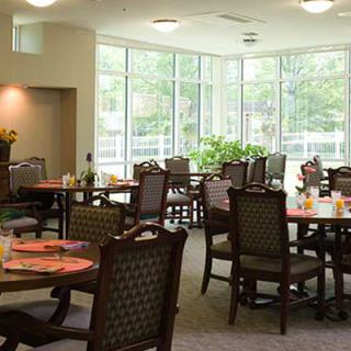 A spacious dining area with multiple tables and chairs, illuminated by natural light through large windows.
