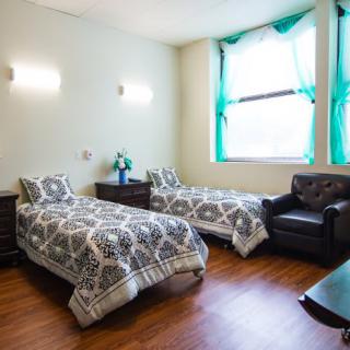 A cozy bedroom with two twin beds, a window with green curtains, and comfortable furniture.