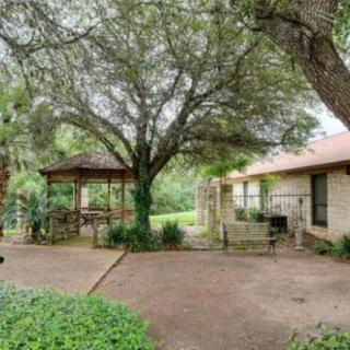 A peaceful backyard with a large tree, gazebo, and adjacent house.