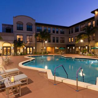 A luxurious outdoor swimming pool at night, surrounded by a well-lit resort building and comfortable deck chairs.