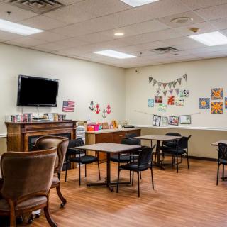 A cozy room with tables and chairs, decorated with artwork and a television mounted on the wall.