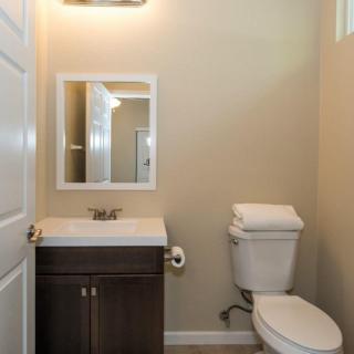A small, neatly arranged bathroom with a sink, mirror, toilet, and a light fixture.