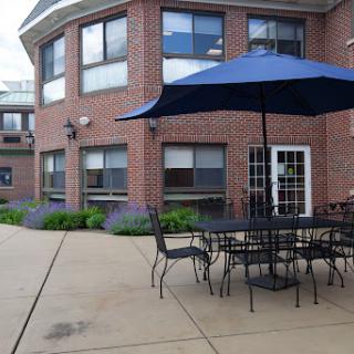 A cozy outdoor patio area featuring tables and chairs under a large blue umbrella, adjacent to a brick building.