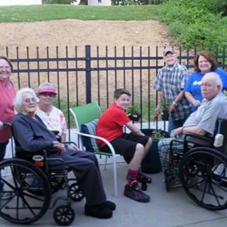 A group of people, including elderly individuals in wheelchairs, enjoy an outdoor gathering.
