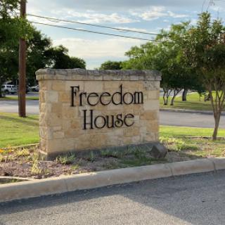 Entrance sign for Freedom House, surrounded by greenery.