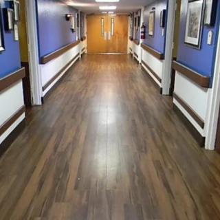 A long, empty hallway with wooden flooring and decorated walls leading to double doors.