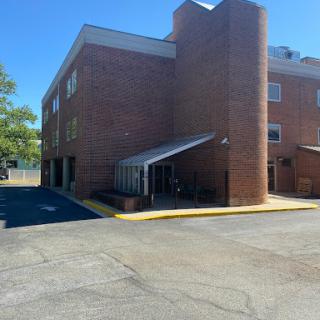 A well-lit brick building with a canopy over the entrance and a parking area.