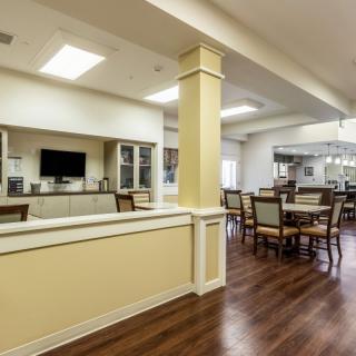 A spacious dining area with wooden floors, tables, and chairs, featuring a television and bright overhead lighting.