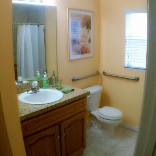 A small bathroom with a sink, toilet, and shower, featuring warm wall colors and decor.