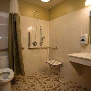An accessible bathroom featuring a walk-in shower with grab bars and a folding seat, designed for safety and convenience.