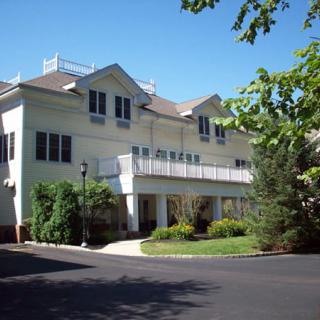 A two-story residential building surrounded by trees and landscaping.