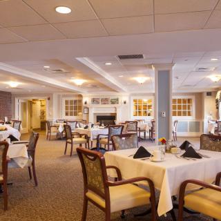 An elegant dining room with neatly arranged tables and chairs, featuring white tablecloths and warm lighting.