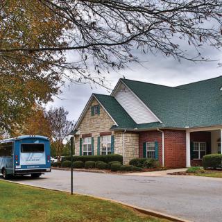 A blue bus parked in front of a suburban building on a cloudy day.