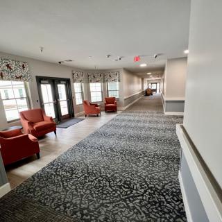 A bright hallway with red chairs and large windows, featuring elegant carpet and decor.