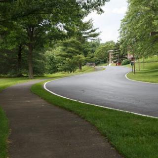 A serene view of a winding road bordered by lush greenery and a pedestrian walkway.
