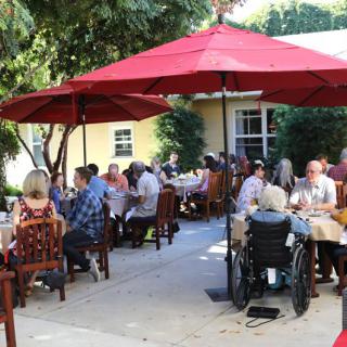 A group of people enjoying a meal together under red umbrellas at an outdoor restaurant.