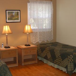 A cozy bedroom setup featuring two beds, matching nightstands with lamps, and a window dressed with a lace curtain.