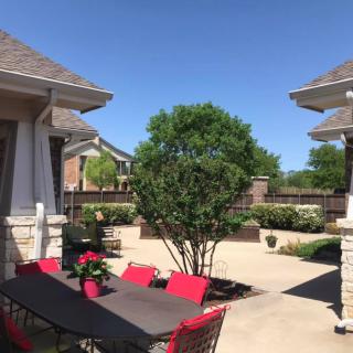 A sunny backyard patio with outdoor furniture, including a table and red chairs, surrounded by houses.