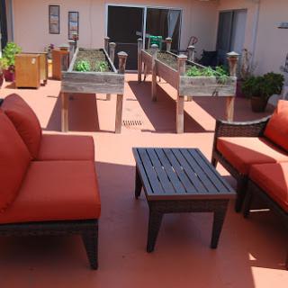 A cozy outdoor seating area with orange cushions and raised garden beds in the background.