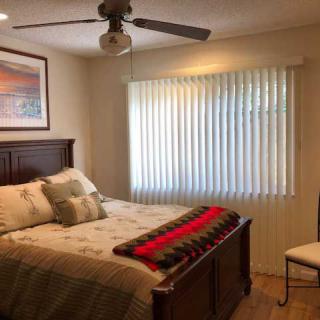 A cozy bedroom featuring a double bed with decorative pillows and a red-striped blanket, complemented by a ceiling fan and window blinds.