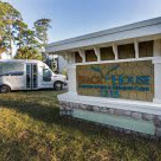 A van is parked near a building with a colorful sign, surrounded by trees.