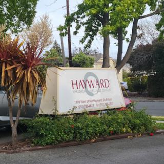 A sign for Hayward surrounded by greenery and urban scenery.