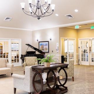 A spacious and elegantly decorated living room featuring a grand piano and chandelier.