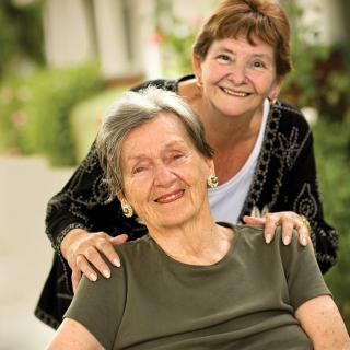 Two elderly women smiling outdoors, enjoying each other's company.