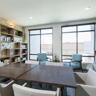 A modern office meeting room with a large table, chairs, bookshelves, and natural light from the windows.