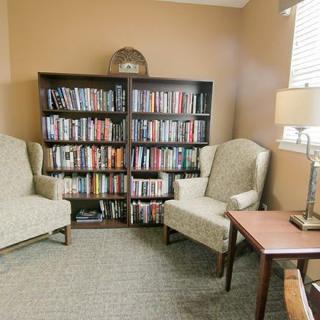 A cozy reading nook with two chairs, a lamp, and a bookshelf filled with books.