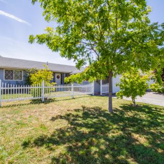 A suburban house with a white fence and green yard featuring a tree.